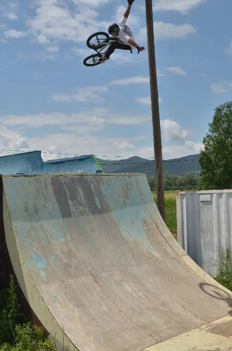 Rider en BMX en saut, une main levée, au-dessus d'une grande courbe en bois usée