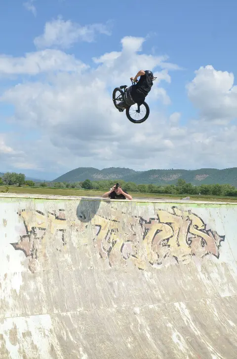 Rider en BMX en saut au-dessus d'une courbe graffée, un photographe sur le rebord, collines derrière