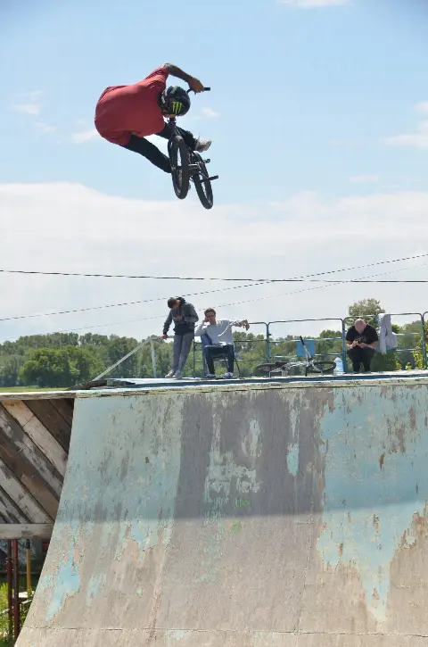 Rider en t-shirt rouge en saut au-dessus d'une rampe usée, spectateurs en haut