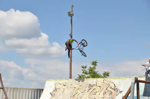 Rider en BMX la tête en bas au-dessus d'une courbe graffée, sous un ciel bleu nuageux