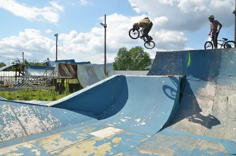 Rider en BMX en saut entre deux modules bleus, un autre rider torse nu attend en haut