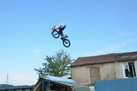 Rider en BMX en saut haut dans le ciel bleu, au-dessus d'un toit de tôle et devant une maison