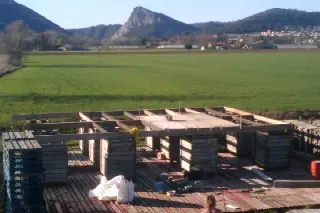 Plancher de palettes et caisses en bois en cours d'assemblage devant un champ, montagnes en arrière-plan