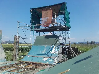 Tour d'échafaudage bâchée au sommet d'une rampe verte et bleue, au milieu des champs