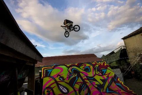 Rider en BMX en plein saut, haut dans le ciel, au-dessus d'un module couvert de graffitis colorés