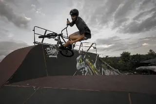 Rider casqué en BMX en saut au-dessus d'un module couvert de graffitis, sous un ciel nuageux