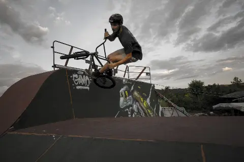 Rider casqué en BMX en saut au-dessus d'un module couvert de graffitis, sous un ciel nuageux