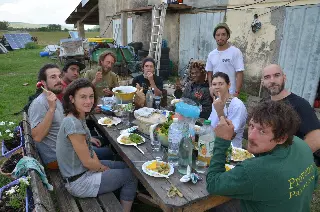 Groupe d'amis attablés en plein air pour un repas devant un bâtiment de ferme