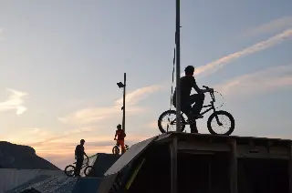 Silhouettes de riders en BMX sur les rampes au coucher du soleil, l'un d'eux en haut d'une plateforme en bois