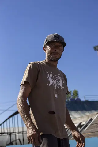Homme en casquette et t-shirt marron à tête de bélier, debout devant les rampes du park sous un ciel bleu