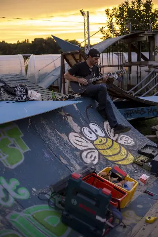 Homme jouant de la guitare électrique en haut d'une rampe peinte au coucher du soleil, caisses à outils au premier plan