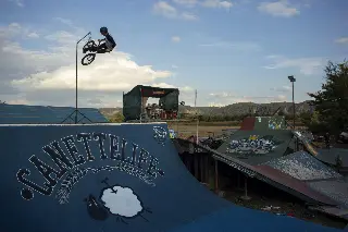 Rider en BMX en saut au-dessus d'une rampe bleue marquée « Canettelife », vue sur l'ensemble du park