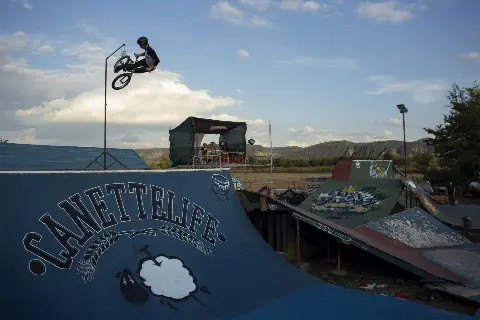 Rider en BMX en saut au-dessus d'une rampe bleue marquée « Canettelife », vue sur l'ensemble du park