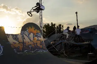 Rider en BMX en saut au-dessus d'une courbe graffée au coucher du soleil, d'autres riders attendent sur une plateforme