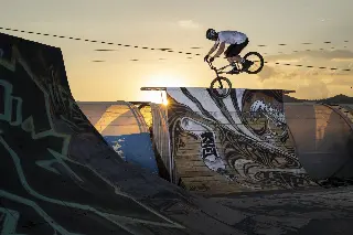 Rider en BMX en saut au-dessus d'une rampe graffée, à contre-jour au coucher du soleil