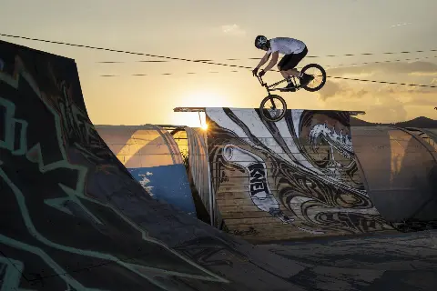 Rider en BMX en saut au-dessus d'une rampe graffée, à contre-jour au coucher du soleil