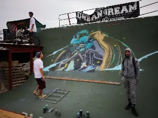 Fresque d'un rider en BMX peinte sur une rampe verte, trois personnes devant et bombes de peinture au sol
