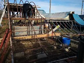 Personne grimpant sur l'ossature métallique d'une rampe en construction, rampes bleues derrière