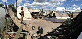 Personne avec une perceuse sur une rampe en bois en chantier, outils au sol et autres modules derrière