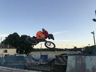 Rider en short orange en saut au-dessus des modules bleus du park, champ et soleil couchant derrière