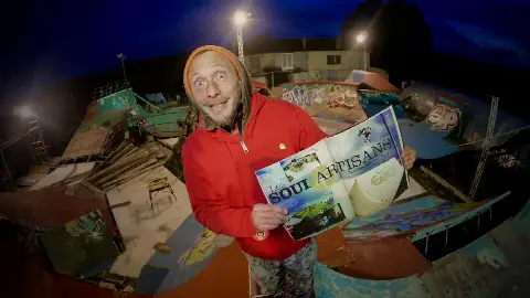 Homme en sweat rouge montrant de nuit dans le park un magazine ouvert sur un article « Soul Artisans »