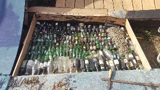 Bac en bois rempli de bouteilles en verre vides couchées, clous rouillés au premier plan