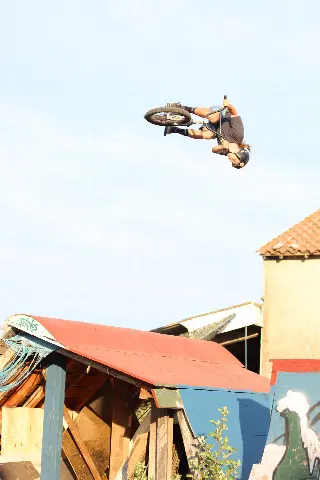 Rider en BMX la tête en bas, haut dans le ciel, au-dessus d'un module à toit de tôle rouge