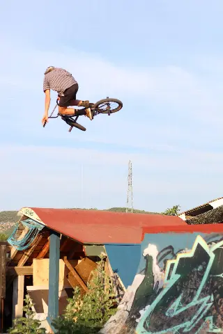 Rider en BMX en saut au-dessus d'un module à toit de tôle rouge, pylône électrique au loin