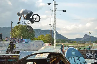 Rider en BMX en saut au-dessus des modules, pylône d'éclairage, spectateurs et montagnes en arrière-plan