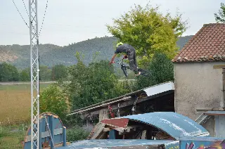 Rider casqué en BMX en saut au-dessus de cabanes en bois et de toits de tôle, collines boisées derrière