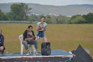 Femme tenant un bébé près d'un homme assis sur une chaise en plastique, sur une plateforme face aux champs