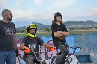 Trois riders côte à côte, l'un sur son BMX avec un casque intégral, devant une rampe graffée