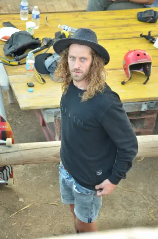 Homme aux cheveux longs et chapeau noir devant une table couverte de casques et d'affaires