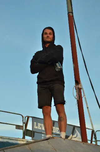 Homme en sweat noir à capuche, bras croisés, debout en haut d'une rampe, vu en contre-plongée