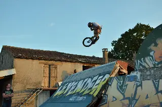 Rider en BMX en saut au-dessus d'une rampe marquée « Levendeep », devant une vieille bâtisse