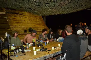 Riders et invités attablés en soirée sous un filet de camouflage, appareil photo sur la table