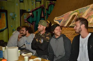 Groupe d'hommes souriants assis à table devant des rampes couvertes de graffitis