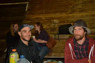 Deux hommes attablés au premier plan et deux femmes qui discutent derrière, devant une paroi en bois