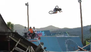 Rider en BMX à l'horizontale haut au-dessus des rampes bleues, riders spectateurs et collines derrière