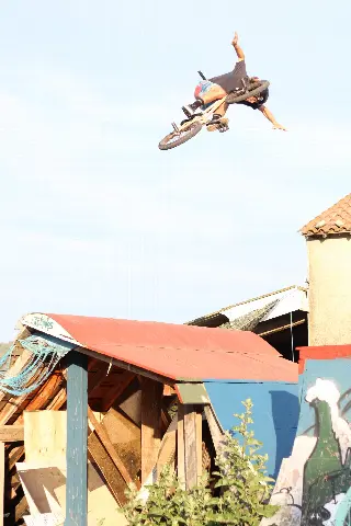 Rider en BMX en plein saut, un bras tendu vers le ciel, au-dessus d'un module à toit de tôle rouge