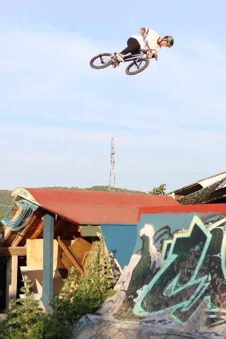 Rider casqué en BMX, à l'horizontale en plein saut, au-dessus d'un module à toit rouge