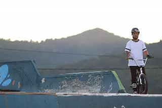 Rider casqué debout avec son BMX en haut d'une rampe bleue, collines en arrière-plan