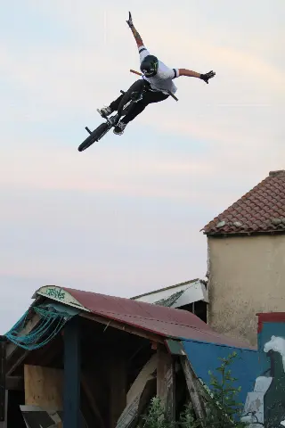 Rider casqué en saut, bras écartés au-dessus de son BMX, au-dessus d'un module à toit rouge