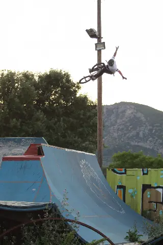 Rider en BMX en saut, un bras levé, au-dessus d'une grande rampe bleue, montagne rocheuse derrière