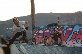 Deux riders casqués avec leurs BMX en haut d'une rampe, devant un mur graffé