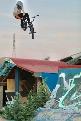Rider casqué en saut, BMX presque à la verticale, au-dessus d'un module à toit rouge