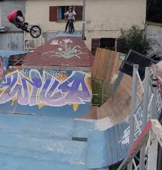 Rider en saut au-dessus d'un module peint de fleurs, un autre rider attend en haut, rampes graffées