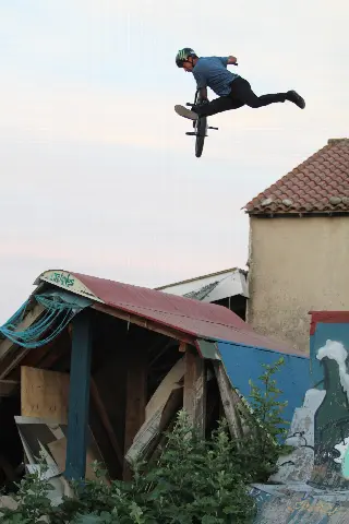Rider en saut, jambes tendues à l'arrière de son BMX, au-dessus d'un module à toit rouge
