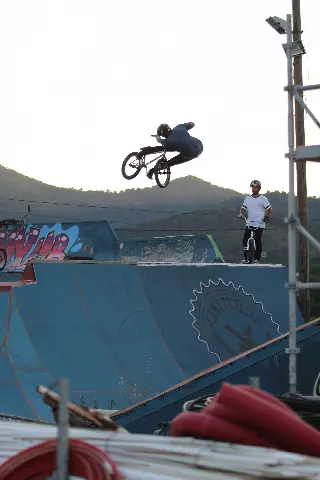 Rider en BMX en saut au-dessus d'une rampe bleue, un autre rider l'observe depuis le haut
