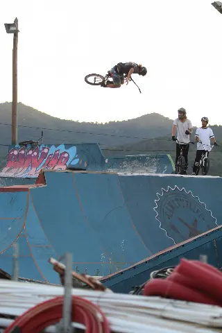 Rider à l'horizontale en saut au-dessus d'une rampe bleue, deux riders casqués regardent depuis le haut